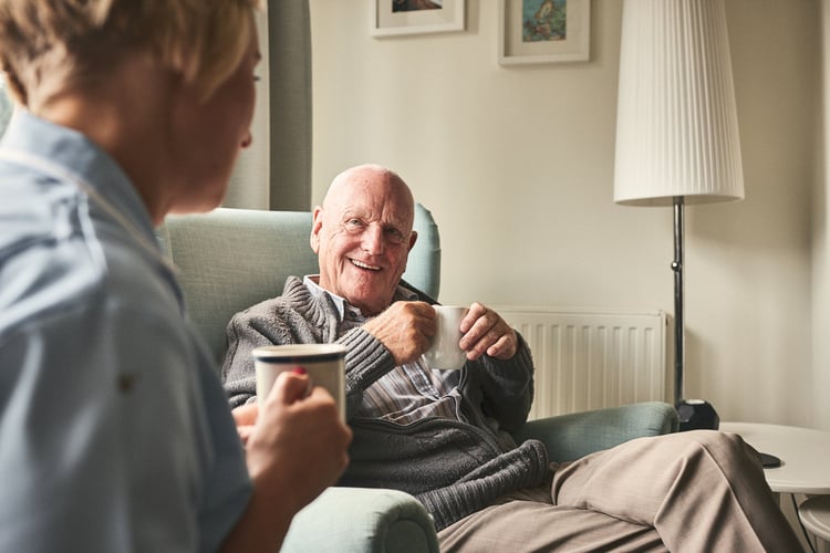 Smiling old man having a cup of tea in his living room